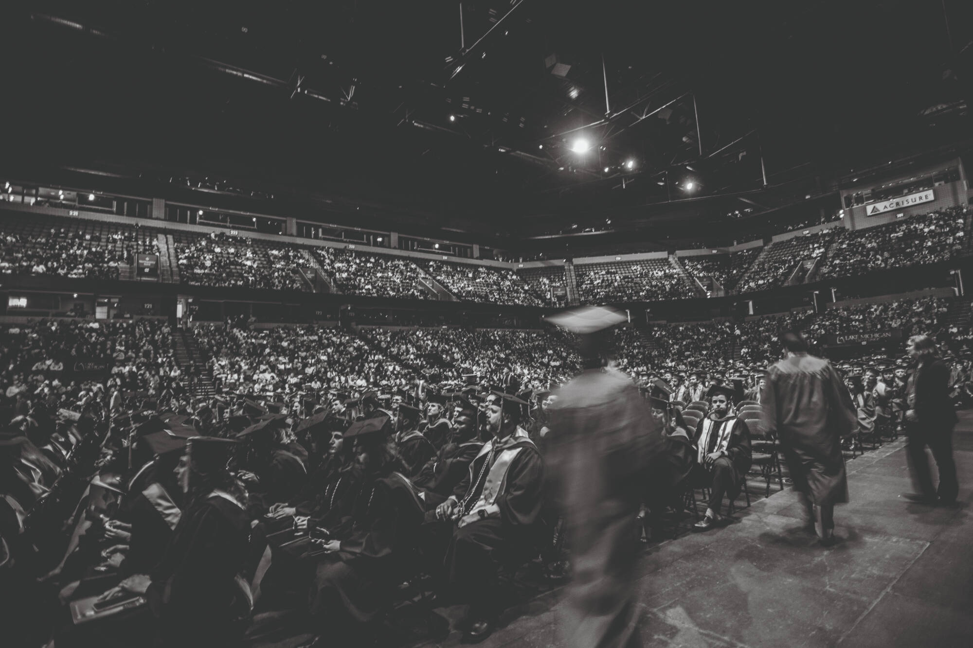 A full stadium of graduates and attendees with a graduate walking down the aisle